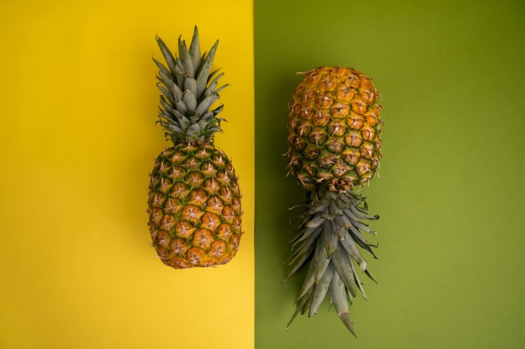 Top view of two pineapples on vibrant yellow and green background showcasing fresh tropical fruit.